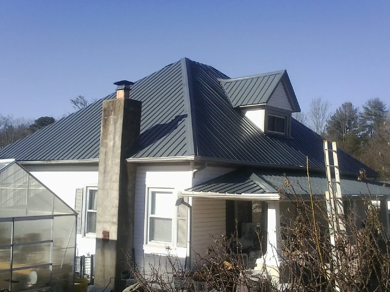Dark blue standing seam metal roof on a white farmhouse with dormer — Slate & Tile Roof Repair by Roofing Brothers in Oakwood