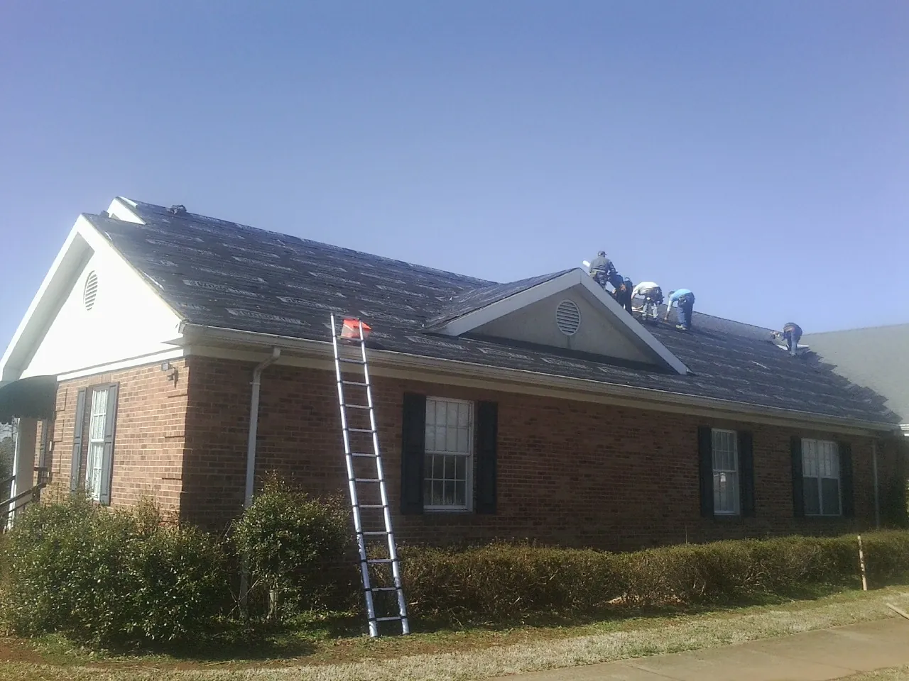 Crew tearing shingles off a brick ranch roof with a ladder set — Emergency Roof Repair work by our crew in Oakwood