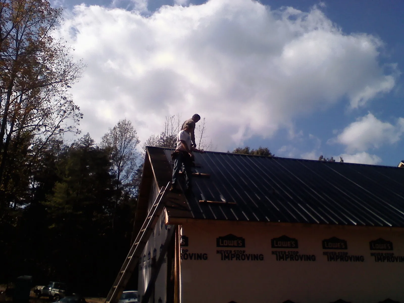 Roofer fastening dark metal panels high against a cloudy sky, from a Roof Inspection job in Oakwood