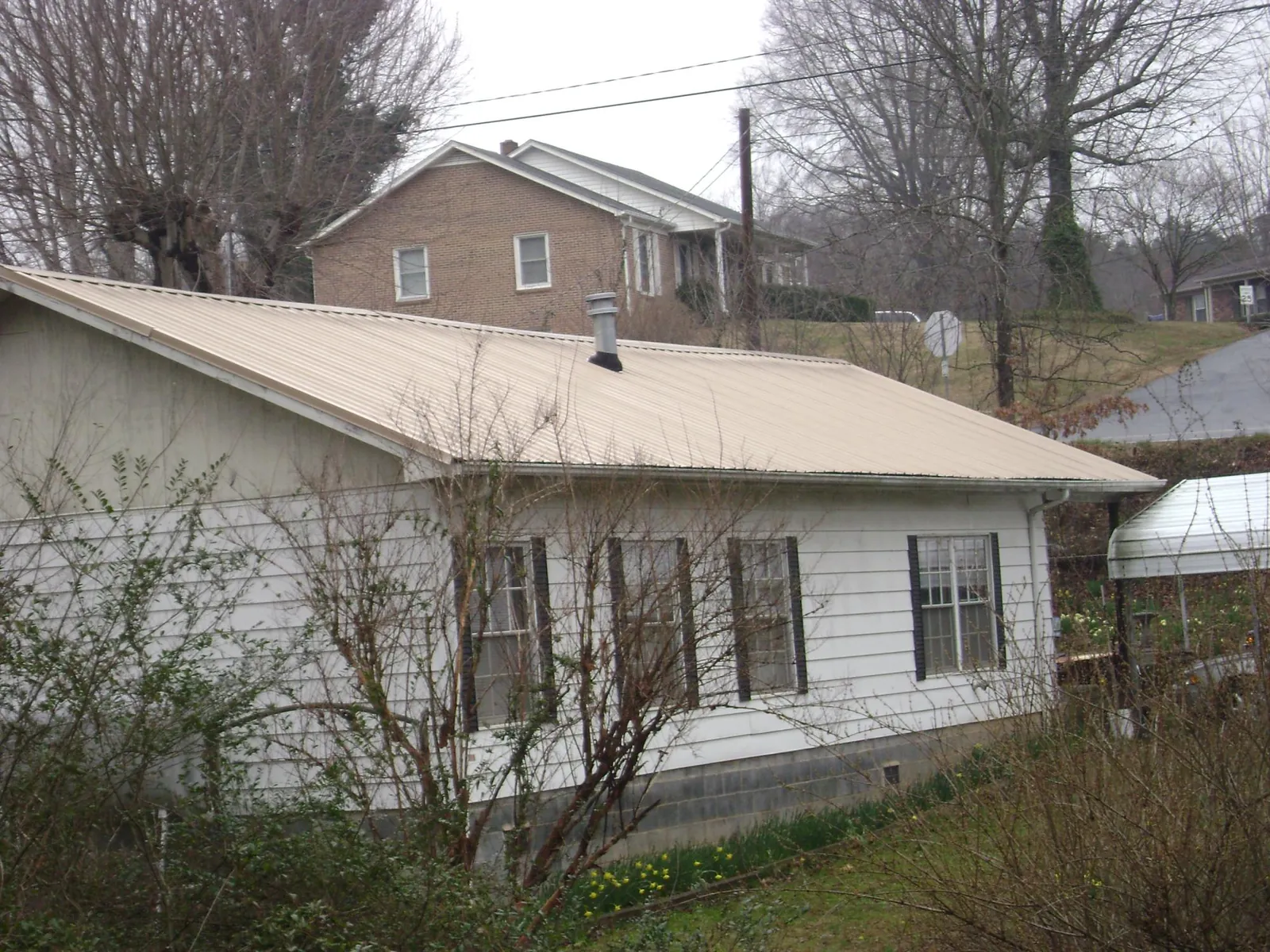 Tan metal roof on a white sided house set into a hillside — Commercial Roofing by Roofing Brothers in Oakwood