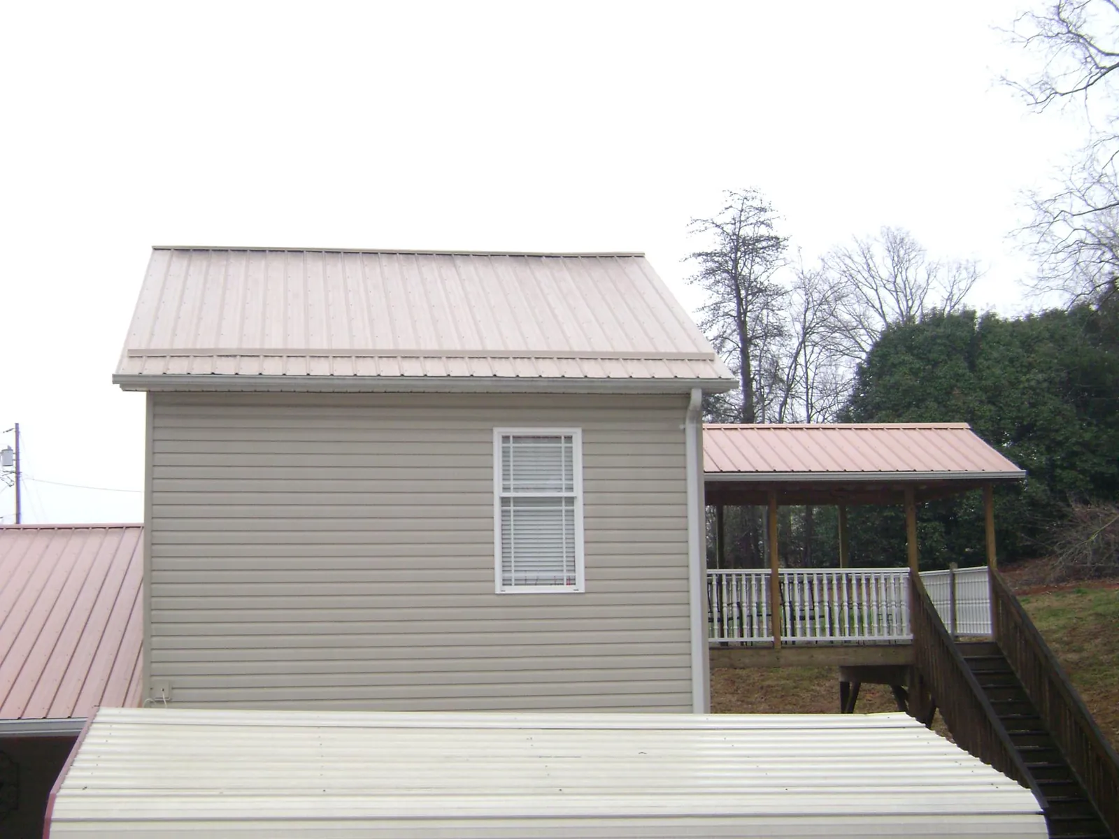 Tan metal roofs on a two story addition and attached porch, from a Roof Replacement job in Oakwood